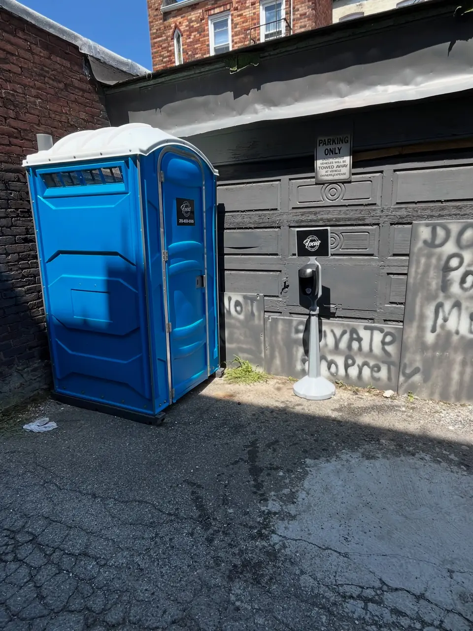 Blue porta potty in a paved alley beside a jobsite