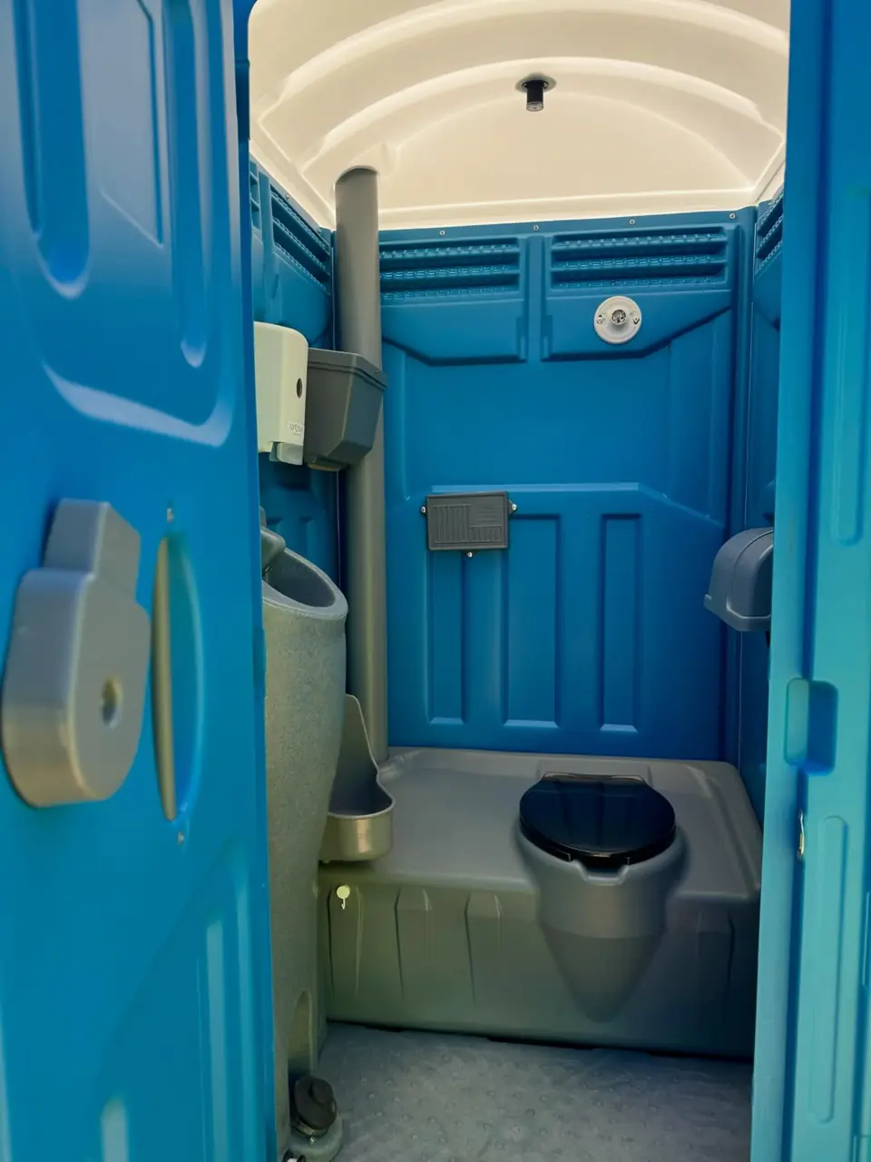 Inside a blue standard porta potty showing the urinal and sanitizer dispenser