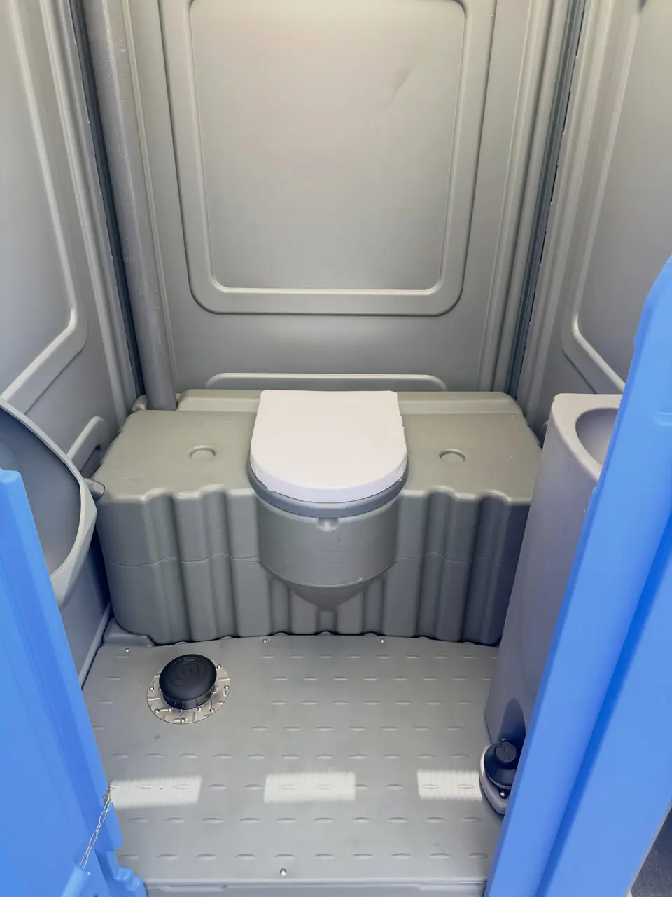 Clean gray interior of a serviced porta potty with toilet paper stocked