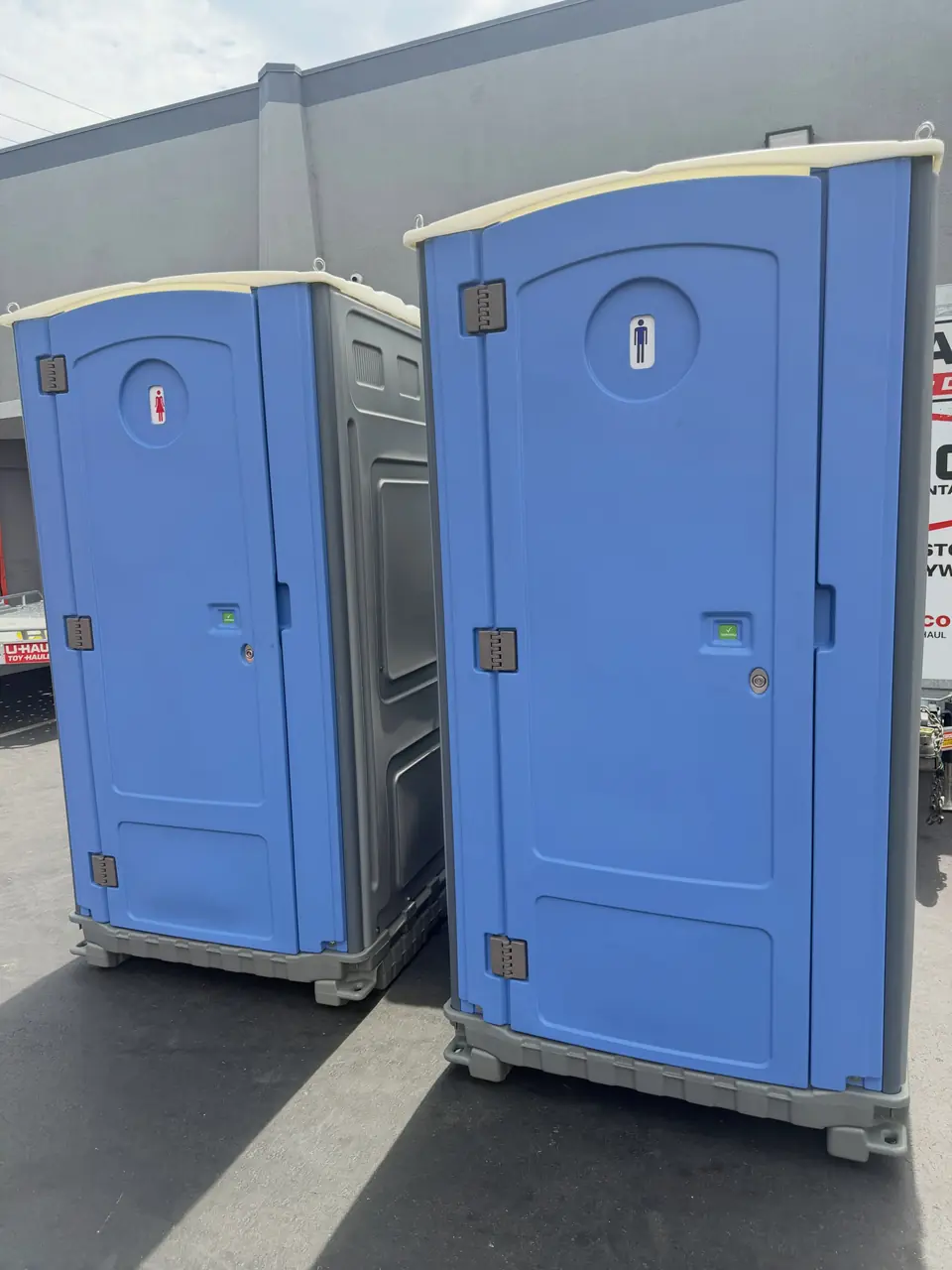 Two blue standard porta potties on a driveway